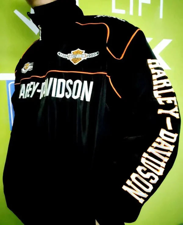 Someone wearing the Vintage Harley Davidson Jacket, featuring bold white and orange lettering on the chest and sleeve, stands against a green background accented with white text and shapes.
