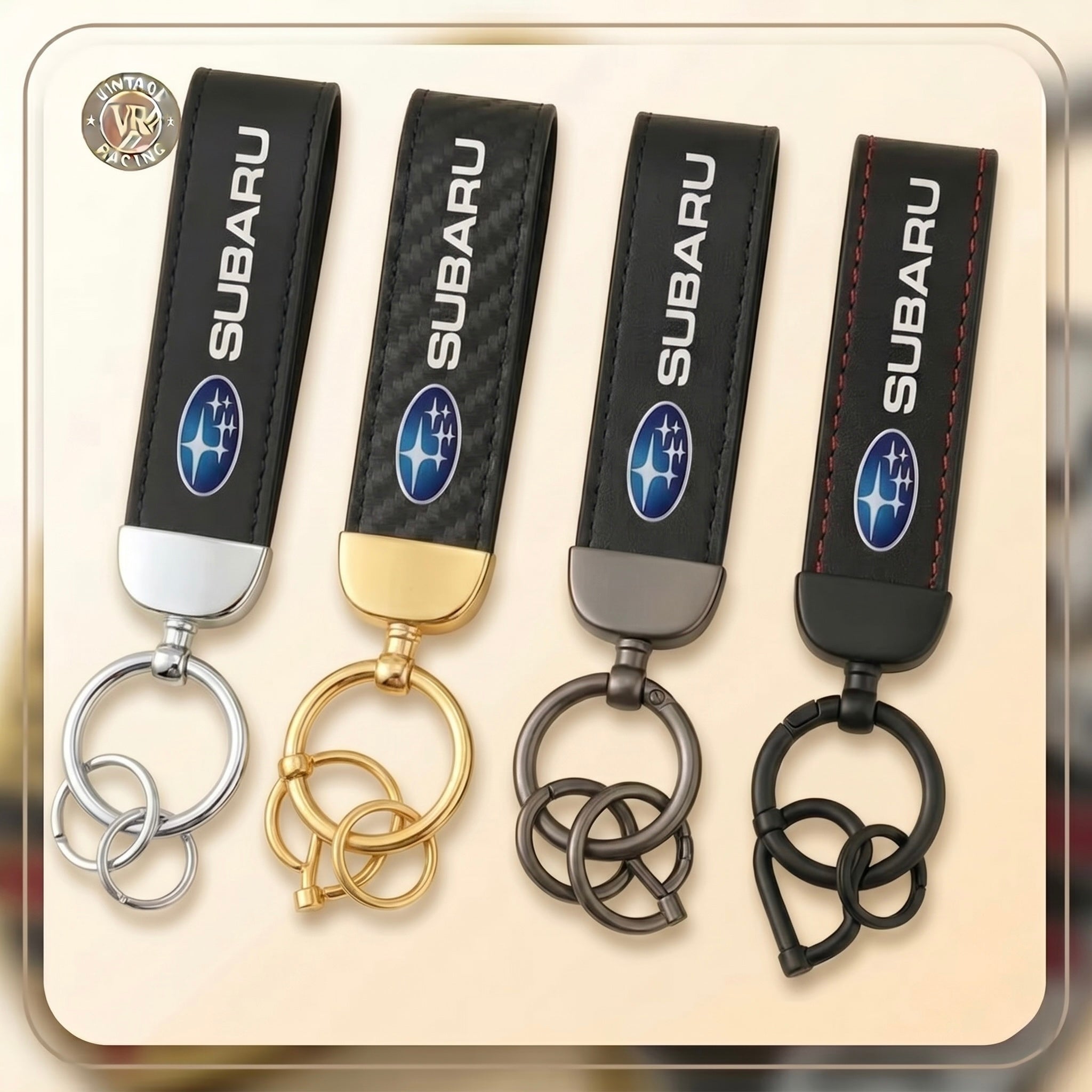 Four Subaru Keychains in silver, gold, gunmetal, and black finishes are displayed side by side on a beige background. Each features the Subaru logo and text—ideal for fans of authentic Subaru accessories.