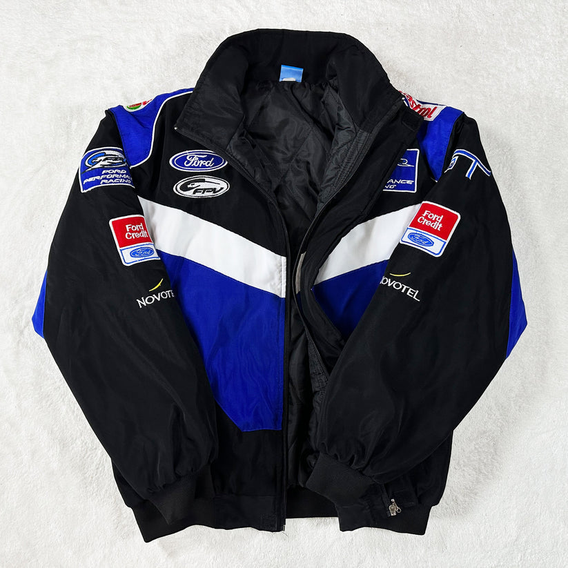 The Ford Vintage Jacket - Performance Edition in black, blue, and white features racing heritage with Ford and Fort Chiswell sponsor logos on the chest, sleeves, and shoulders, displayed on a white surface.