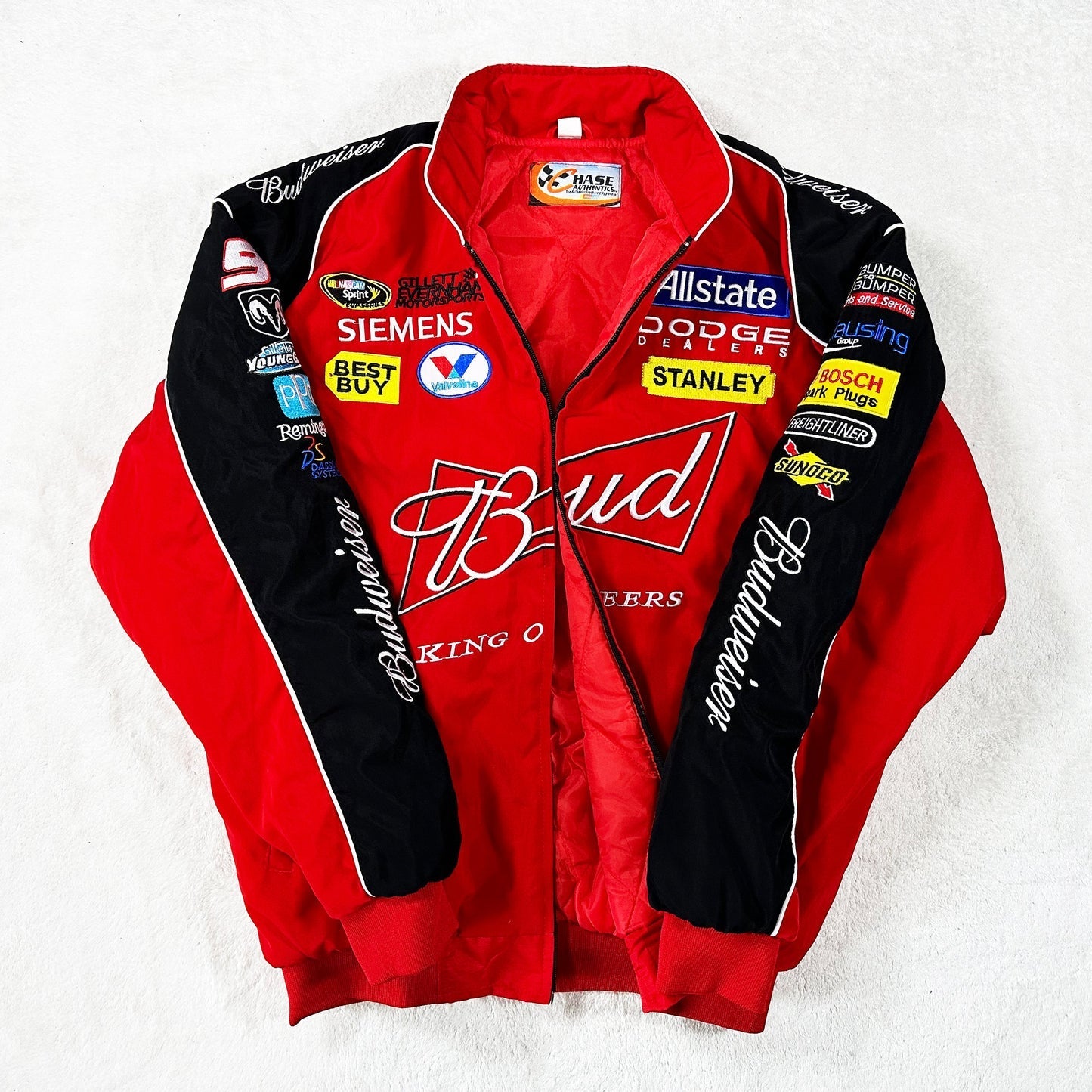 The Budweiser Racing Vintage Jacket - NASCAR Red Edition features striking red and black colors with sponsor patches from Dodge, Allstate, Best Buy, Stanley, Siemens, and more—displayed here on a white surface.
