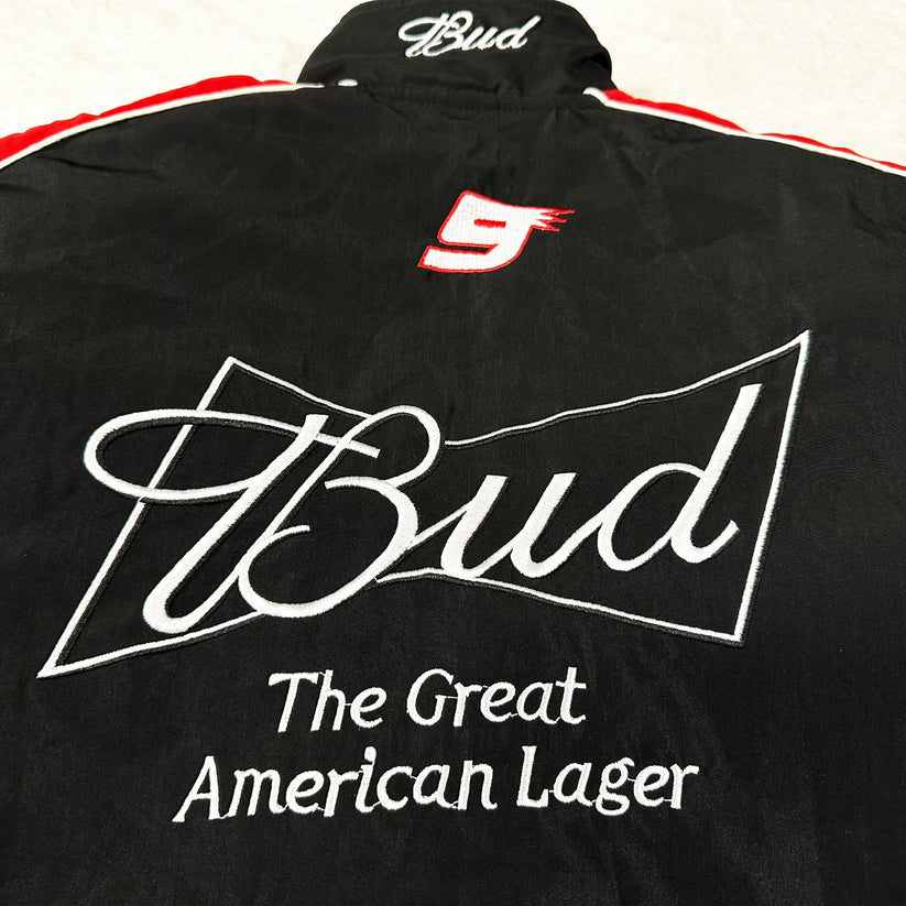The Budweiser Vintage Racing Jacket - NASCAR Black Edition is a black jacket with red and white accents, featuring embroidered “Bud” in white, a red number 9, and the slogan “The Great American Lager.”.