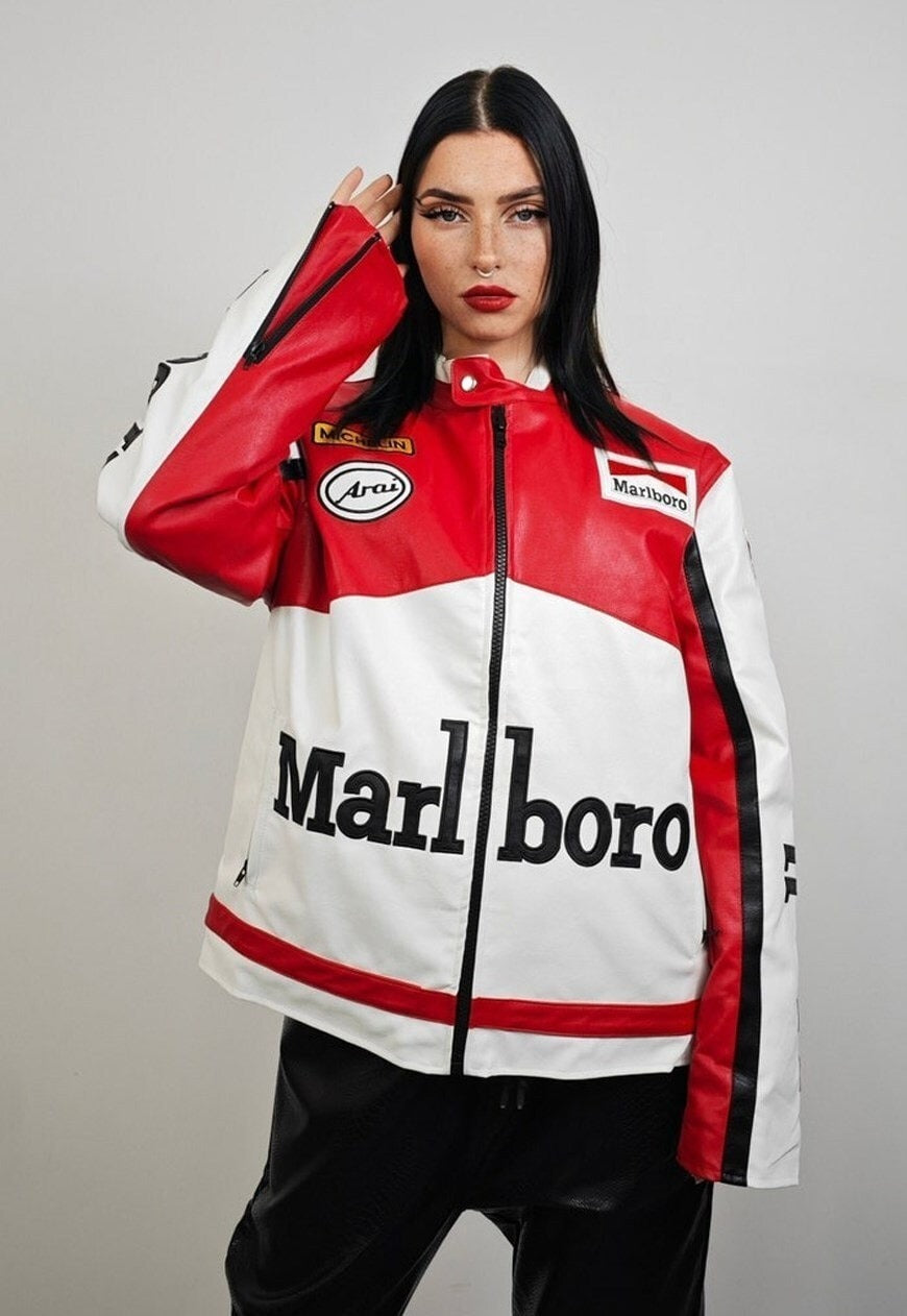 A woman with long dark hair wears the Marlboro Racing Leather Jacket in red, white, and black with bold branding and racing patches, standing against a plain light background.