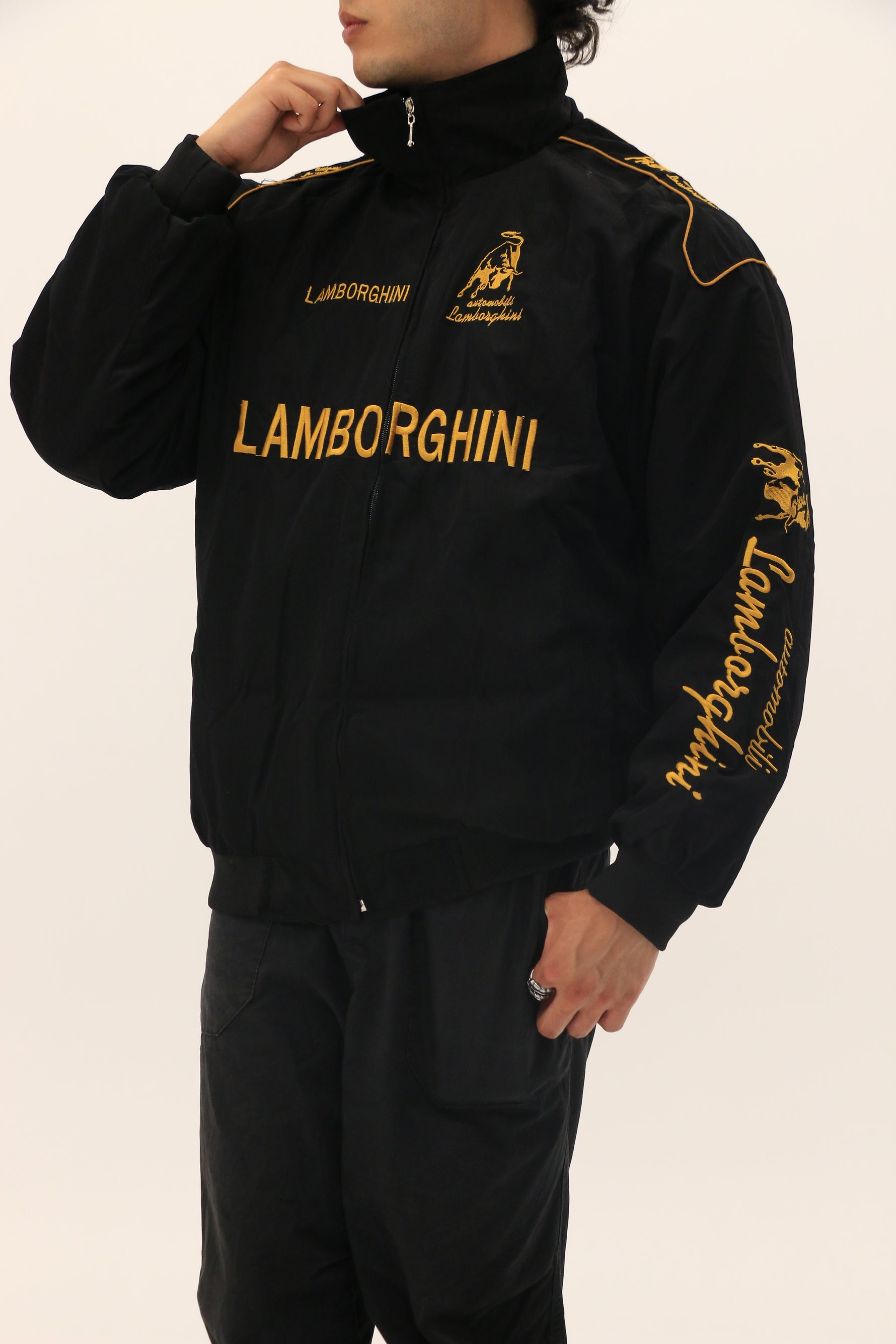 A person wears the Lamborghini Vintage Racing Jacket, featuring yellow embroidery and logos on the chest, sleeve, and collar—ideal for motorsport fans—while standing against a plain light background.