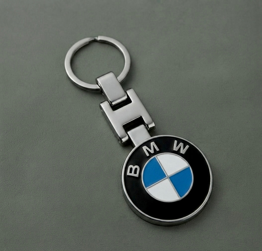 The BMW Keychain, featuring a metallic design with the iconic round BMW roundel in blue, white, and black segments, rests on a sleek gray surface—an ideal accessory for car enthusiasts.
