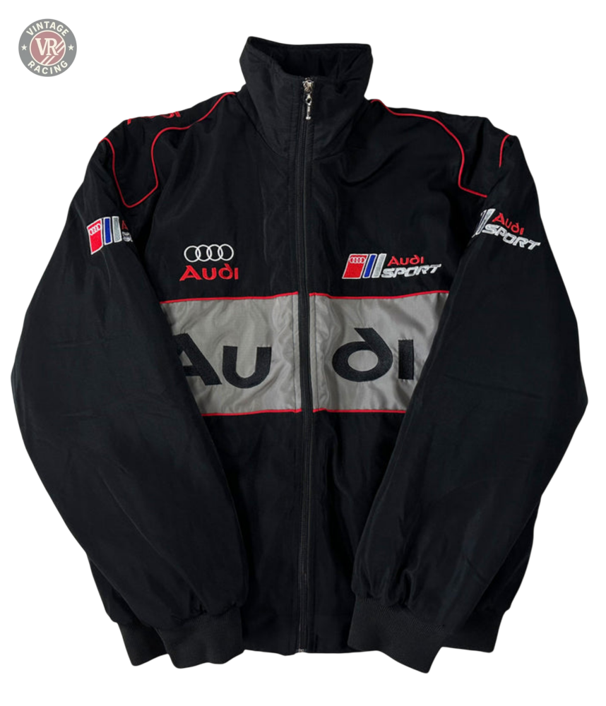 The Audi Vintage Racing Jacket, in black with red and white accents, features chest, sleeve, and back logos plus a central gray stripe with the Audi name. This vintage motorsport jacket is shown zipped up and laid flat.