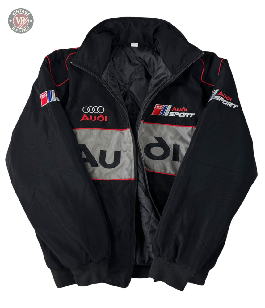 The Audi Vintage Racing Jacket in black with red and silver accents showcases multiple Audi logos and text on the front, sleeves, and chest—highlighting classic Quattro heritage style against a white background.