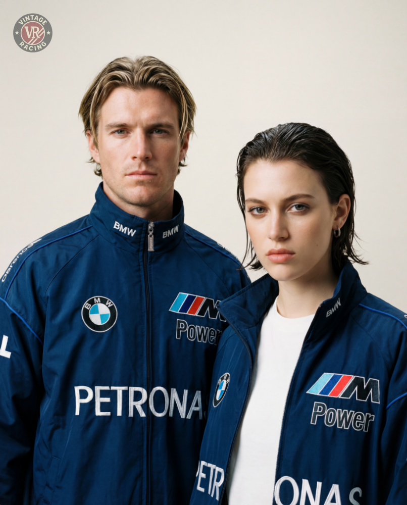 A man and a woman in BMW F1 Vintage Racing Jacket - Classic Edition stand side by side, capturing 2000s Formula 1 nostalgia as they look seriously at the camera against a simple light background.