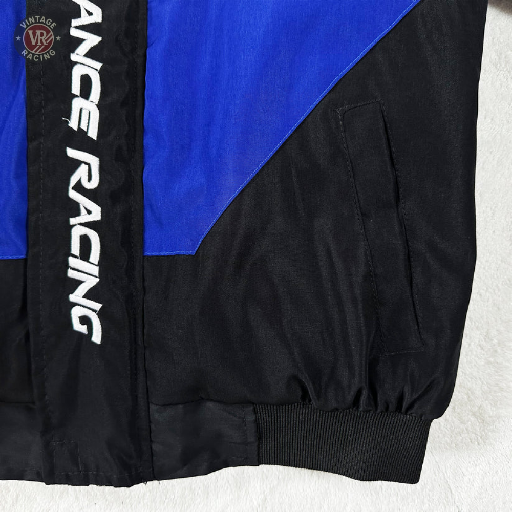Close-up of the Ford Vintage Jacket - Performance Edition with blue and black panels. ANCE RACING is printed vertically on a black strip. Features a side pocket, ribbed cuff, and sleek performance streetwear design.
