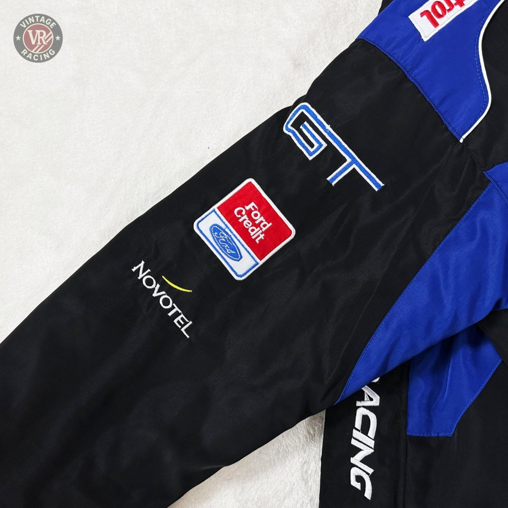 A close-up of the Ford Vintage Jacket - Performance Edition sleeve highlights racing heritage with Novotel, Ford Credit, and Ford sponsor patches, plus GT and RACING text on black and blue fabric.