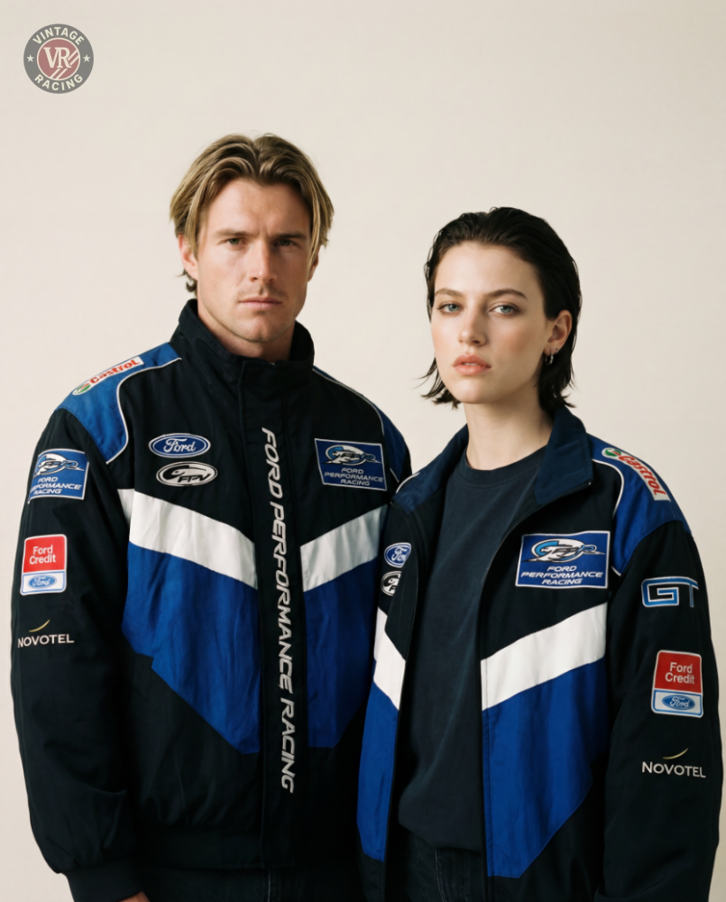 A man and a woman with short hair stand together against a beige background, both wearing matching black and blue Ford Vintage Jacket - Performance Edition streetwear featuring sponsor logos. Their expressions are neutral.