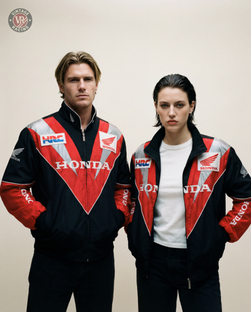 Two people in matching Honda Vintage Racing Jackets—black, red, and silver—stand side by side against a plain light background. One has shoulder-length blond hair and the other short dark hair. Both look serious.