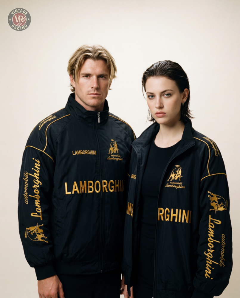 A man and a woman, both motorsport enthusiasts, wear Lamborghini Vintage Racing Jackets with gold lettering and logos, posing side by side against a plain light background.