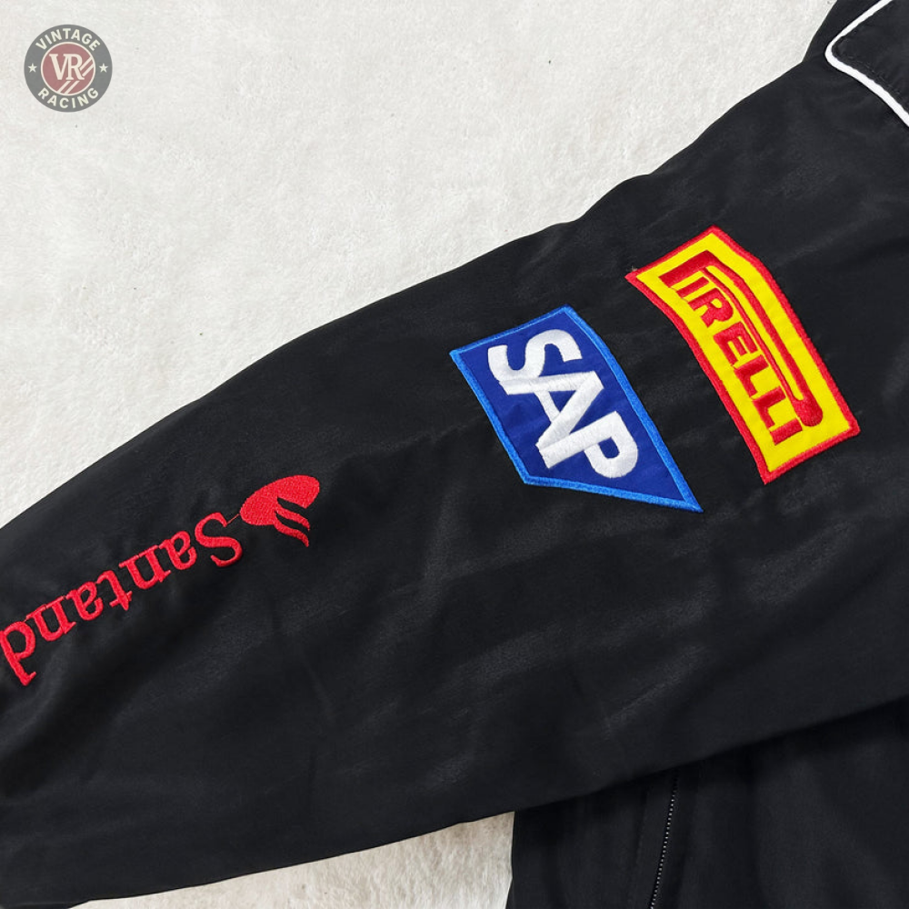 The Mercedes-Benz Santander Vintage Jacket’s black sleeve in stealth racing style showcases embroidered logos: Santander (red), SAP (blue/white), and Pirelli (yellow/red), all set against a light-colored background.