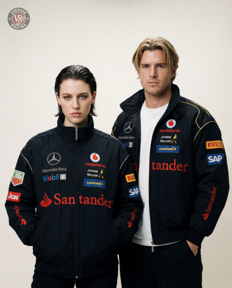 Two people in black racing jackets, including the Mercedes-Benz Santander Vintage Jacket, stand side by side against a plain background, channeling stealth racing style and motorsport heritage as they look directly at the camera.