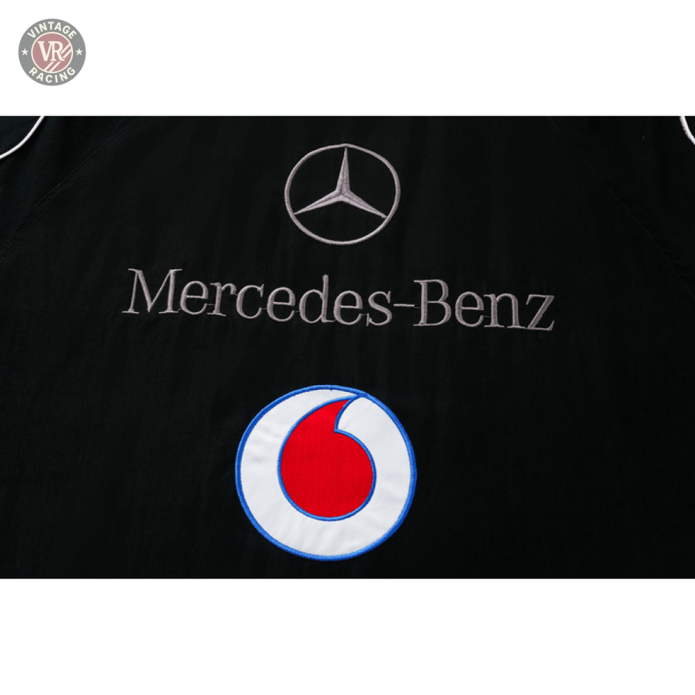 Black fabric features the Mercedes-Benz logo and name, embroidered above a circular Santander logo in red and white with blue outline, on the Mercedes-Benz Santander Vintage Jacket, reflecting motorsport heritage.