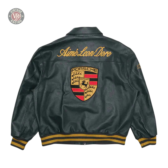 The Porsche Vintage Leather Bomber Jacket - Green Edition features a green leather design with gold Aimé Leon Dore script on the back, a large Porsche crest below, and gold and black striped cuffs and waistband.