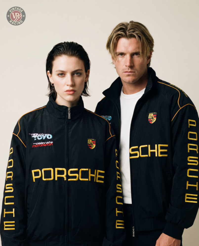 A woman and a man, both with light hair and serious expressions, stand side by side in matching Porsche Vintage Racing Jackets featuring yellow lettering, showcasing retro style against a neutral backdrop.