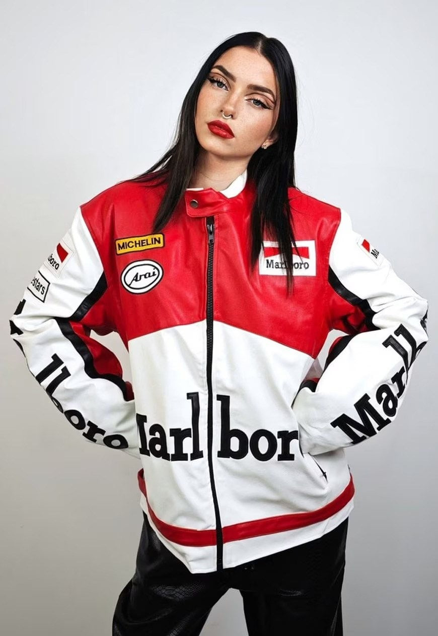 A woman with straight dark hair and bold makeup wears the Marlboro Racing Leather Jacket, inspired by 90s F1 styles with brand patches, standing against a plain light background.