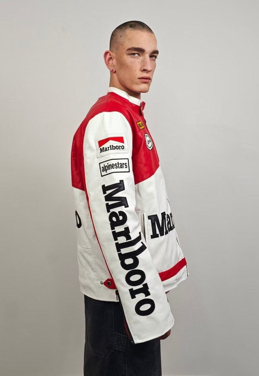 A young man with short hair stands sideways in a Marlboro Racing Leather Jacket with Alpinestars and Ferrari logos, set against a plain light gray background.