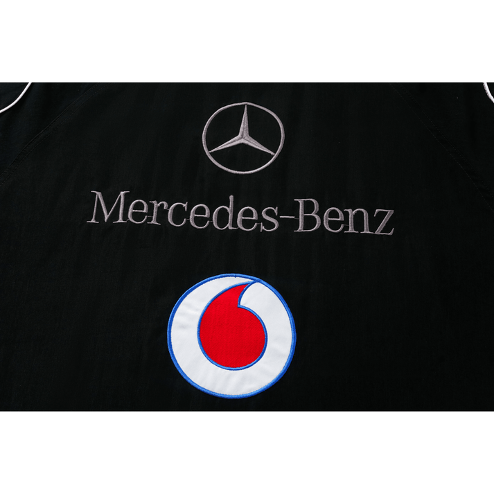 Black fabric features the Mercedes-Benz logo and name, embroidered above a circular Santander logo in red and white with blue outline, on the Mercedes-Benz Santander Vintage Jacket, reflecting motorsport heritage.