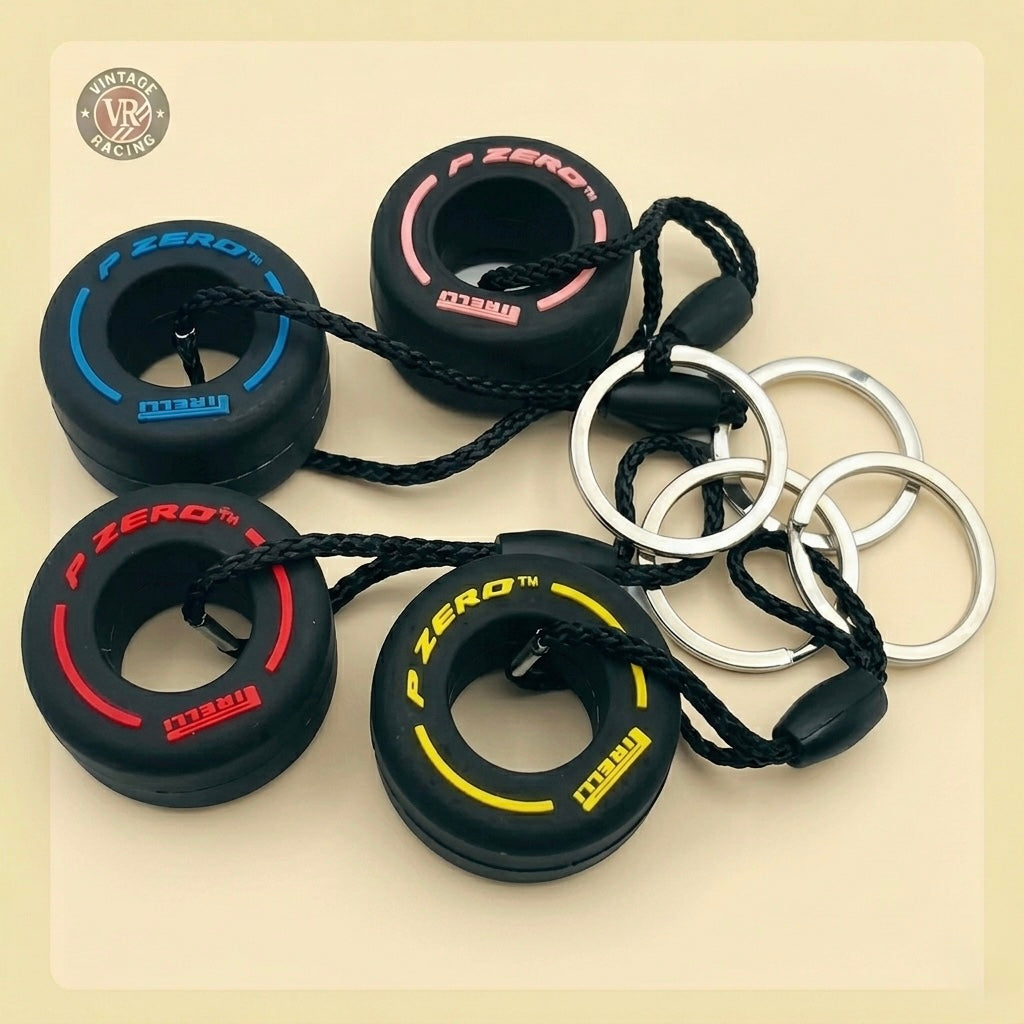 Four Pirelli Tire Keychains in blue, pink, red, and yellow—miniature F1 P Zero tires on metal rings with black cords—make a great gift for F1 fans. Displayed on a light beige surface.