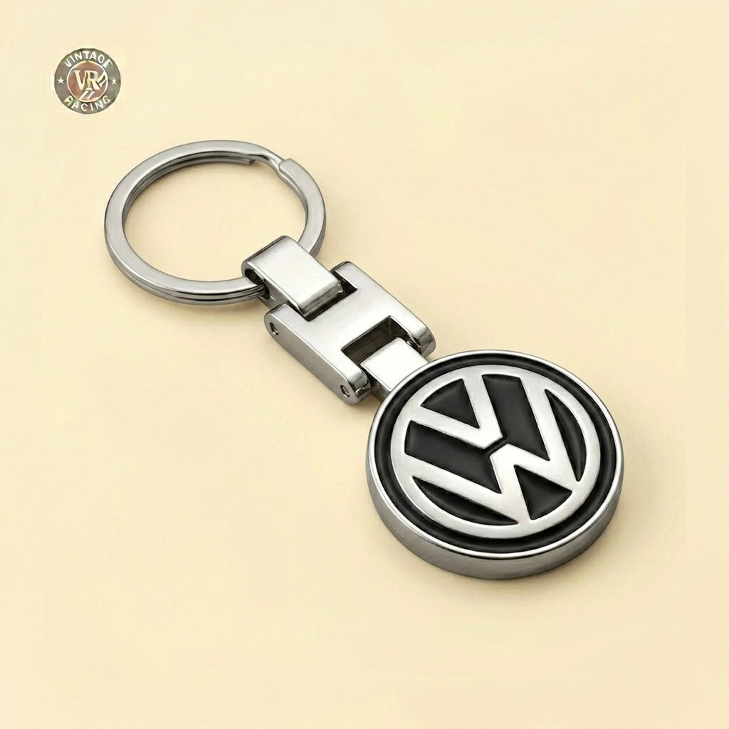 The Volkswagen Keychain features a sleek silver design with the iconic black and silver VW logo, set against a light beige background. A small Vintage Racing emblem appears in the top left—perfect for car enthusiasts.