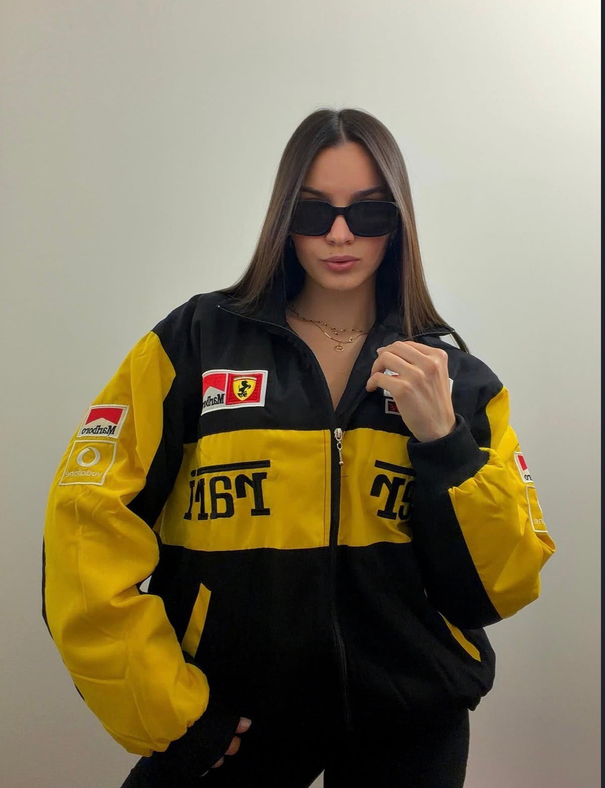 A person wearing a black and yellow Vintage Ferrari Michael Schumacher Jacket with various sponsor logos on the chest and sleeves, and black sunglasses.