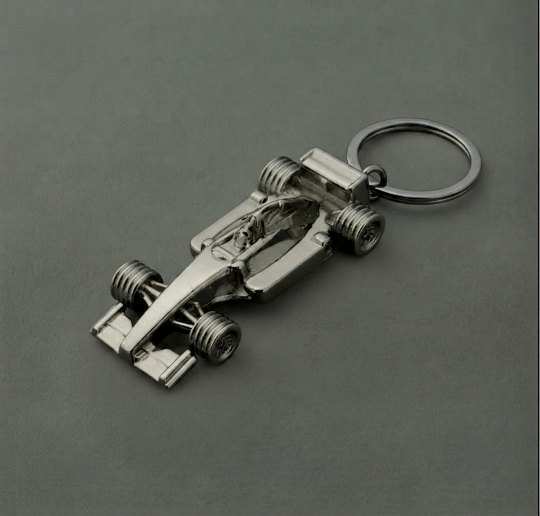 The F1 Racing Car Keychain, designed in the shape of a metallic Formula 1 race car, is showcased on a plain gray surface—making it the perfect gift for motorsport enthusiasts and Formula 1 fans.
