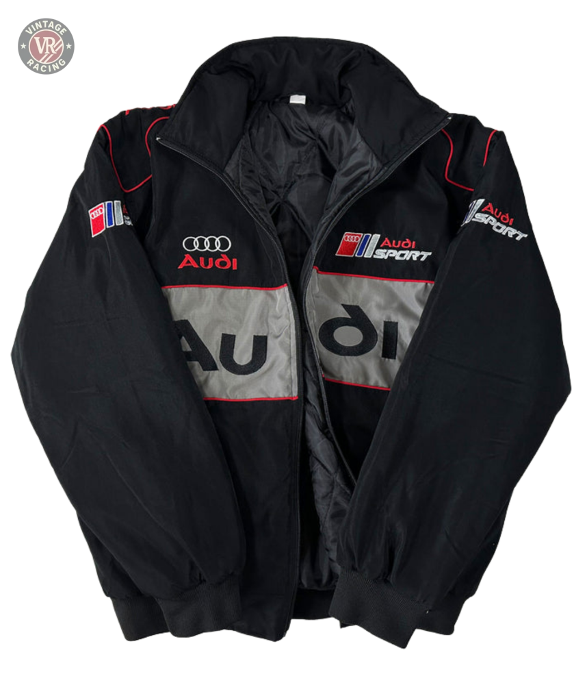 The Audi Vintage Racing Jacket in black with red and silver accents showcases multiple Audi logos and text on the front, sleeves, and chest—highlighting classic Quattro heritage style against a white background.