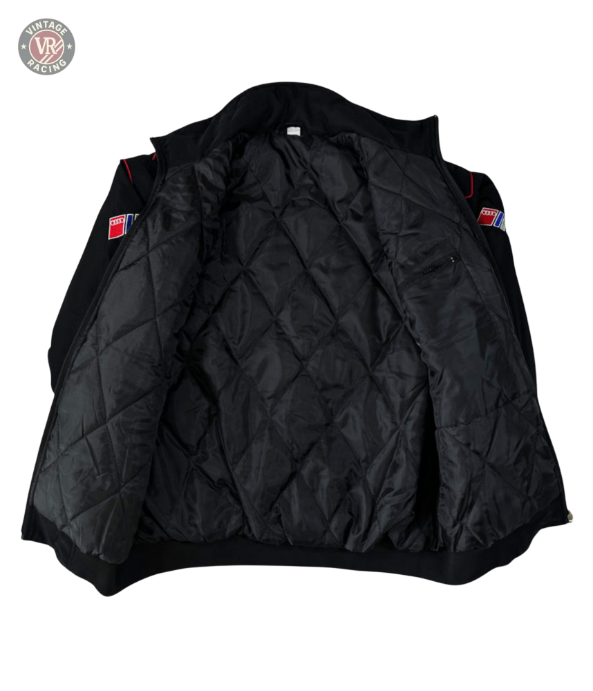 The Audi Vintage Racing Jacket is black with red and blue sleeve patches, features a quilted inner lining, and has a small zippered pocket on the left side—capturing classic vintage motorsport style.
