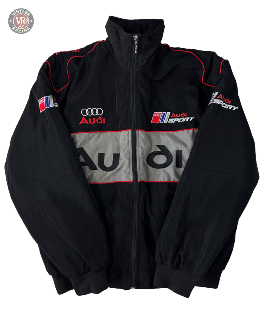 The Audi Vintage Racing Jacket, in black with red and white accents, features chest, sleeve, and back logos plus a central gray stripe with the Audi name. This vintage motorsport jacket is shown zipped up and laid flat.
