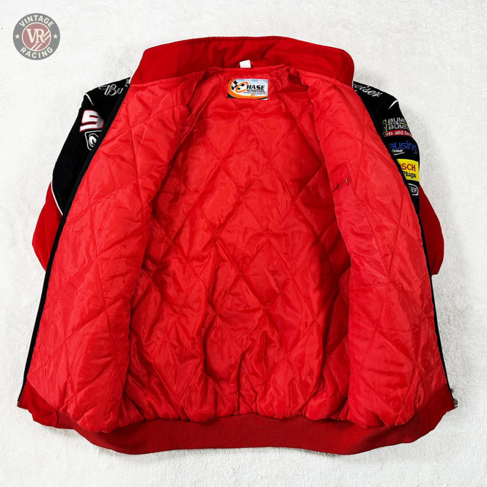 The Budweiser Racing Vintage Jacket - NASCAR Red Edition is displayed open on a white surface, showcasing its quilted red lining and multiple patches and logos on the sleeves and collar for an authentic vintage motorsport vibe.