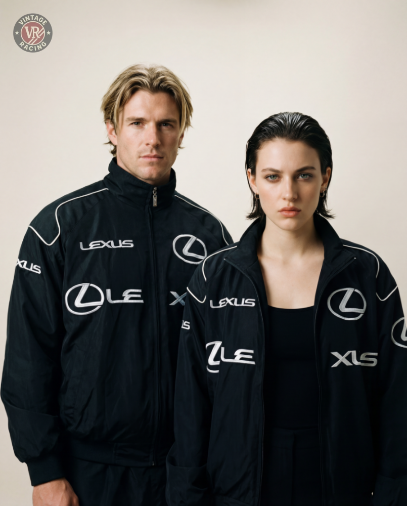 A man and a woman in matching black Lexus Vintage Racing Jackets pose side by side with serious expressions, showcasing motorsport style against a plain, light background.