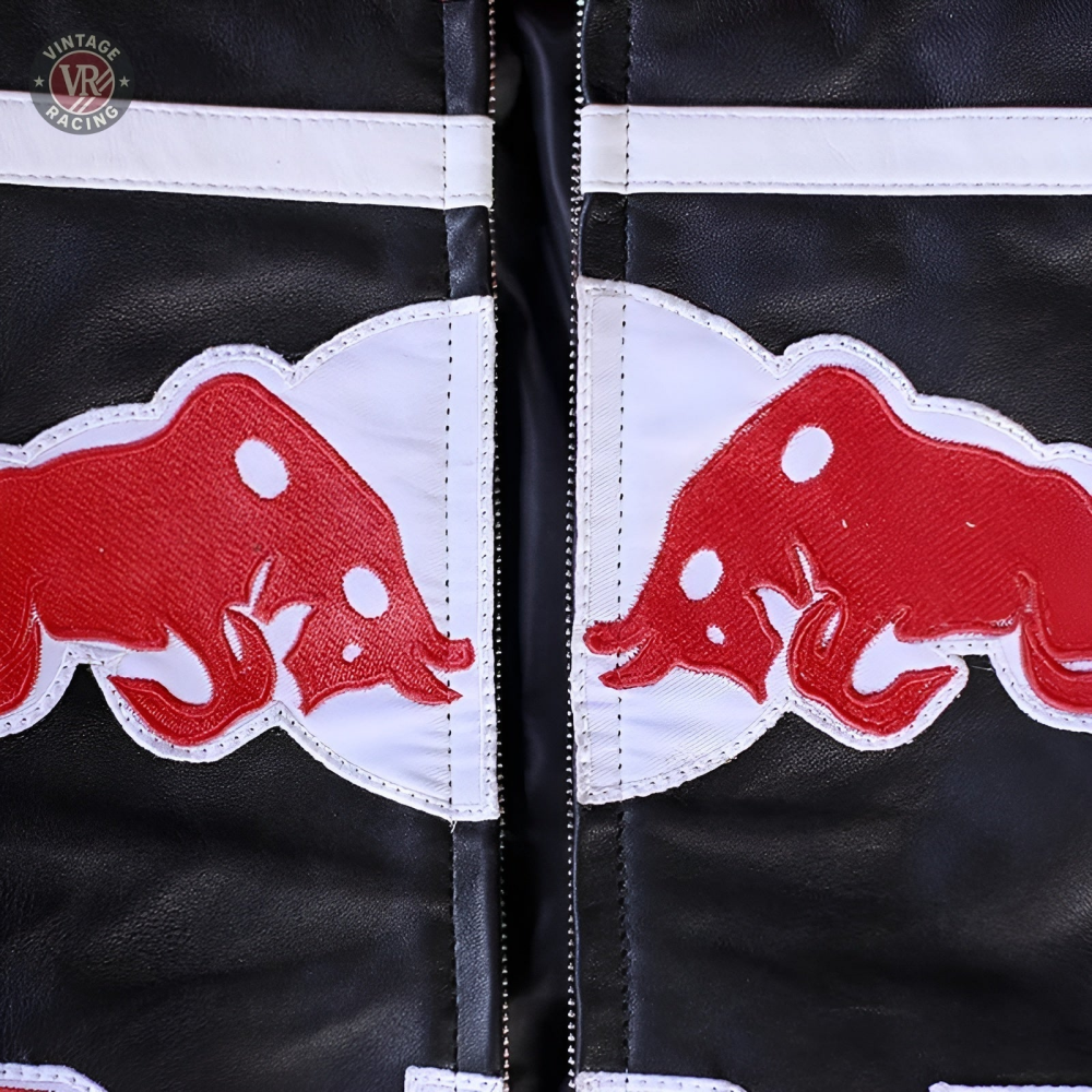 Close-up of the Red Bull Leather Racing Jacket featuring two opposing Red Bull patches on a white background, divided by a central zipper—highlighting its bold racing heritage.