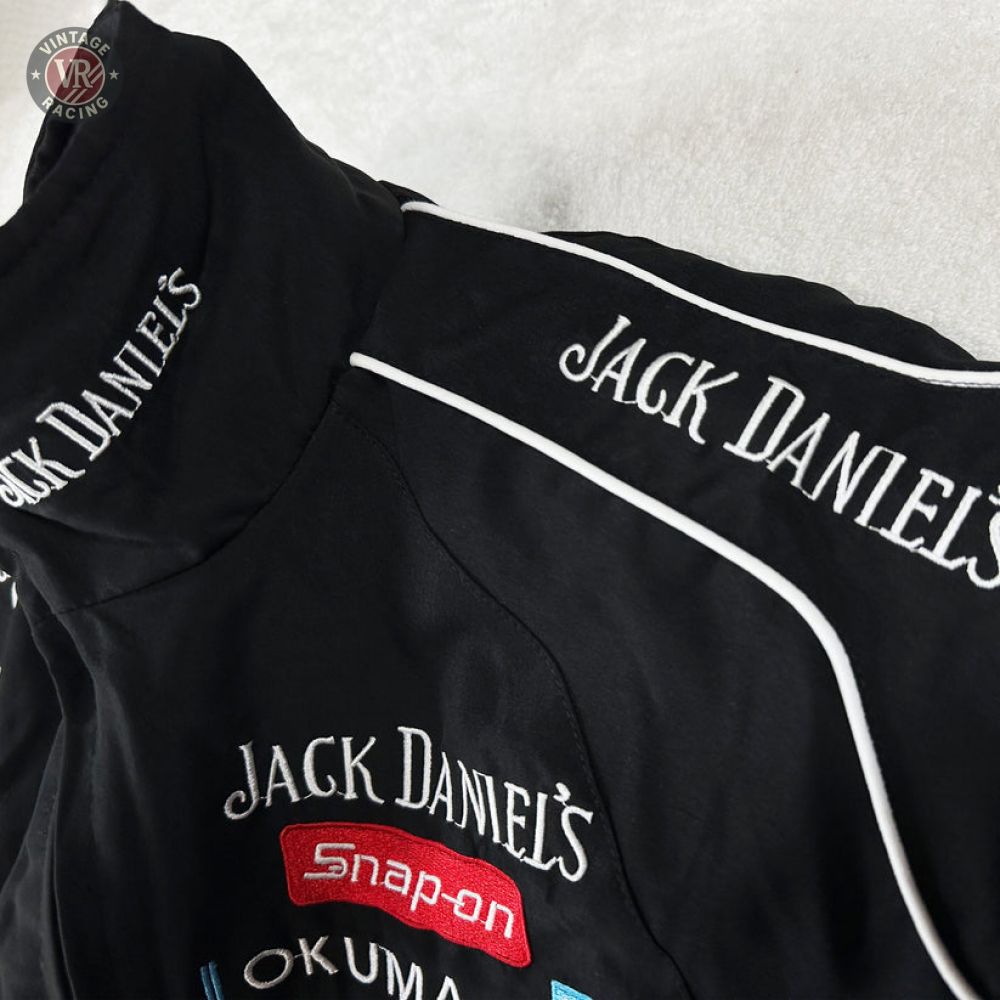 The Sponsored’s Racing Vintage Jacket in black features white Jack Daniels embroidery and Snap-on and OKUMA logos, displayed on a white surface—ideal for motorsport style or adding a bold edge to your streetwear.