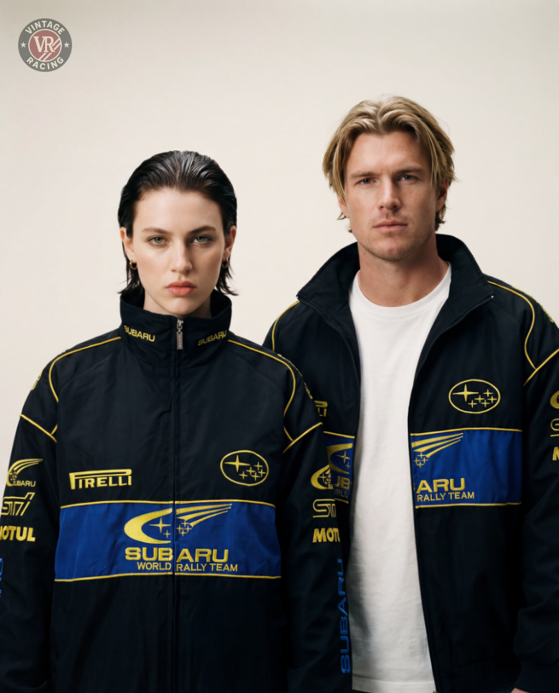 Two people stand side by side against a plain background, each wearing the Subaru Rally Vintage Racing Jacket—one with dark hair, the other blonde with a white shirt—showcasing rally heritage style.