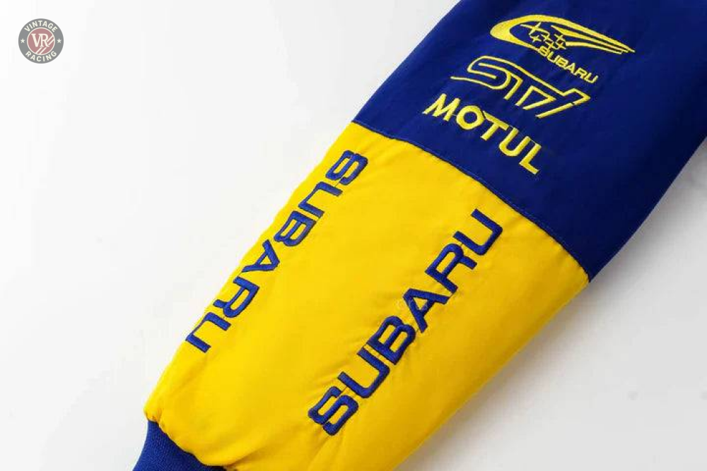 A close-up of the Subaru World Rally Team Vintage Jackets blue and yellow sleeve featuring SUBARU, MOTUL text, the rally car logo, and S17 print—evoking the iconic 555 livery.